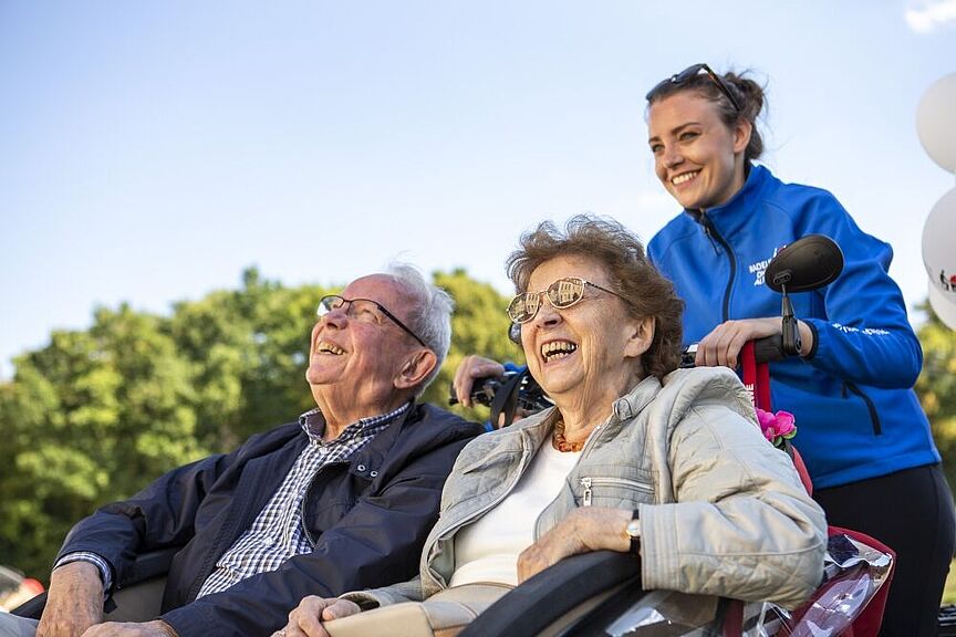 zwei Senioren sitzen lachend in einer Rikscha, die von einer jungen Frau gefahren wird zwei Senioren sitzen lachend in einer Rikscha, die von einer jungen Frau gefahren wird