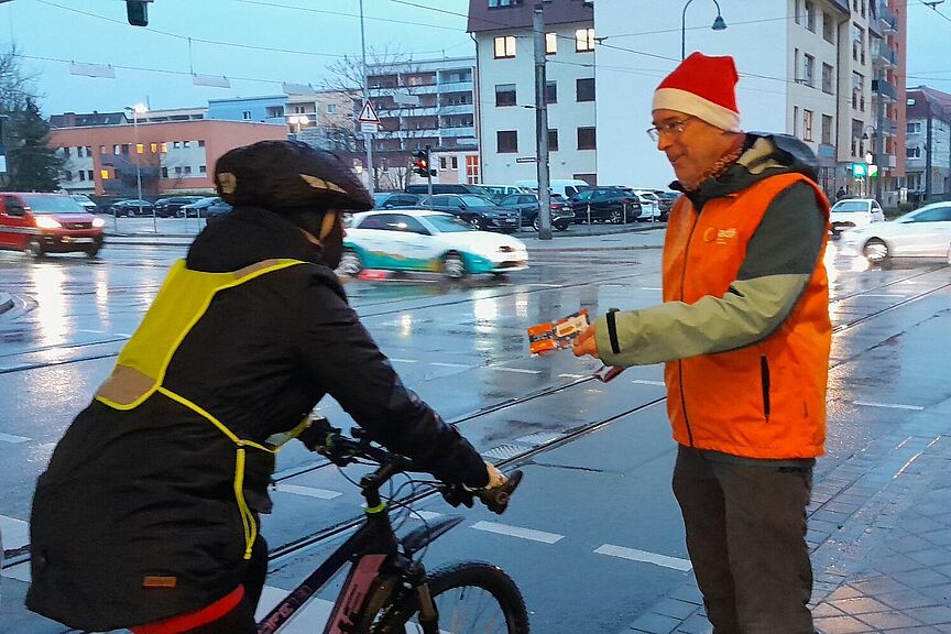 Nikolausaktion 2024 Ein Mann mit Nikolausmütze gibt einer Radfahrerin einen Zimtstern.