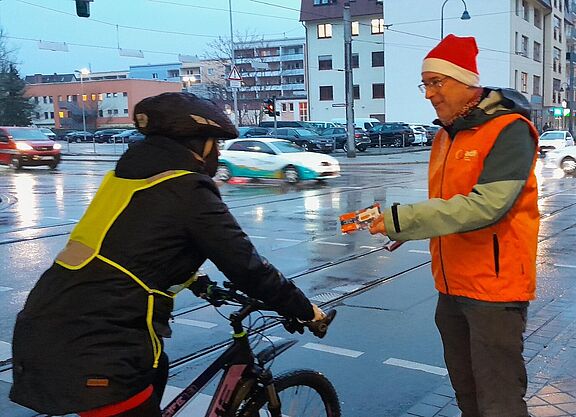 Ein Mann mit Nikolausmütze gibt einer Radfahrerin einen Zimtstern.