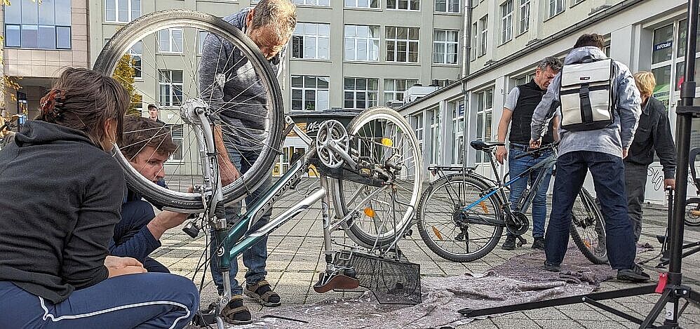 Campusreparaturtag SoSe 2025 Fahrrad steht mit Reifen nach oben auf einer Decke, während drei Menschen es reparieren