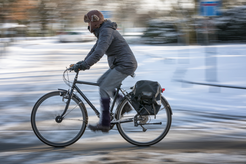 Radfahrer fährt vor einer verschneiten Wiese entlang Radfahrer fährt vor einer verschneiten Wiese entlang