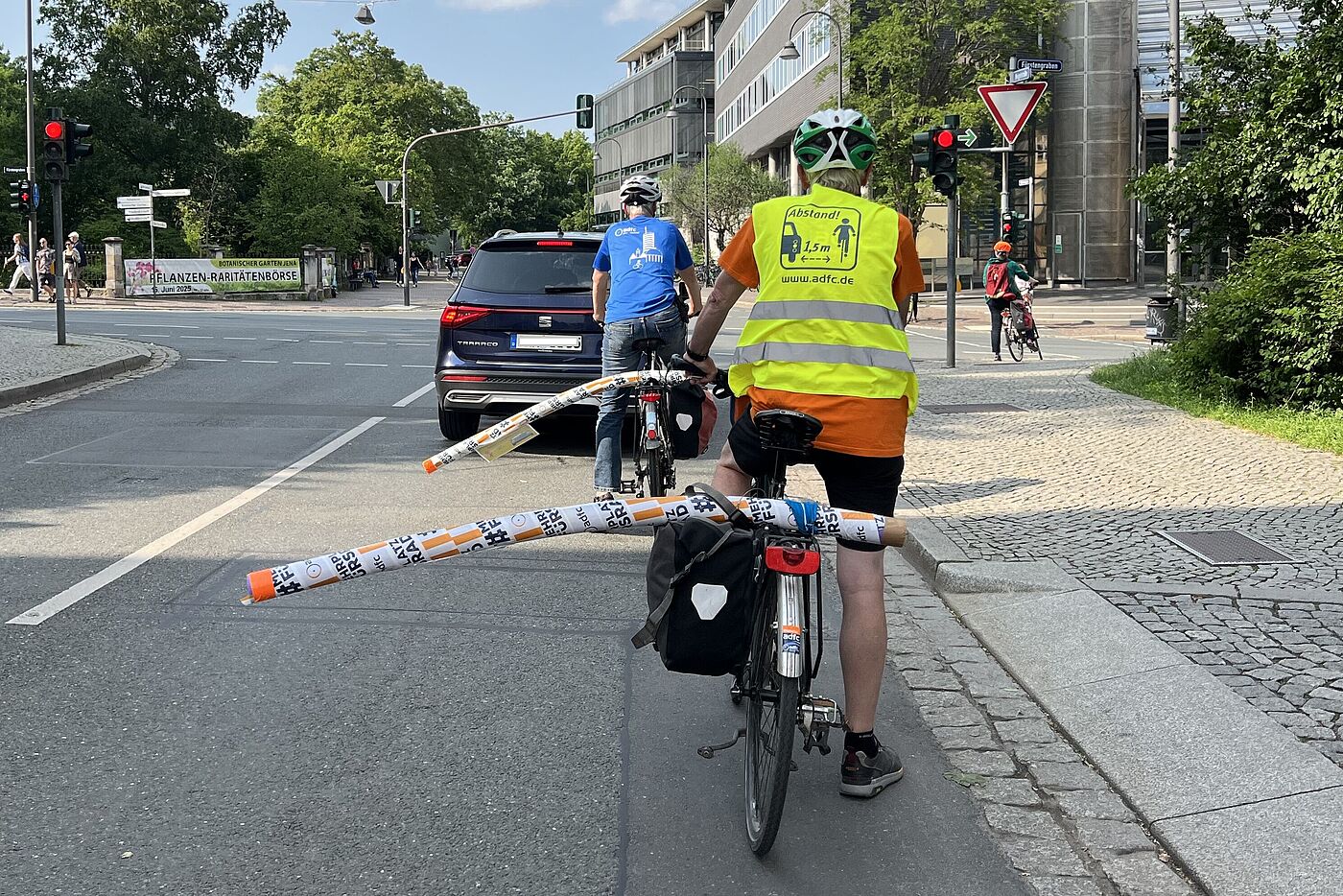 Radfahrende mit Poolnudeln am Gepäckträger, die den Mindestüberholabstand von 1,5 m anzeigen