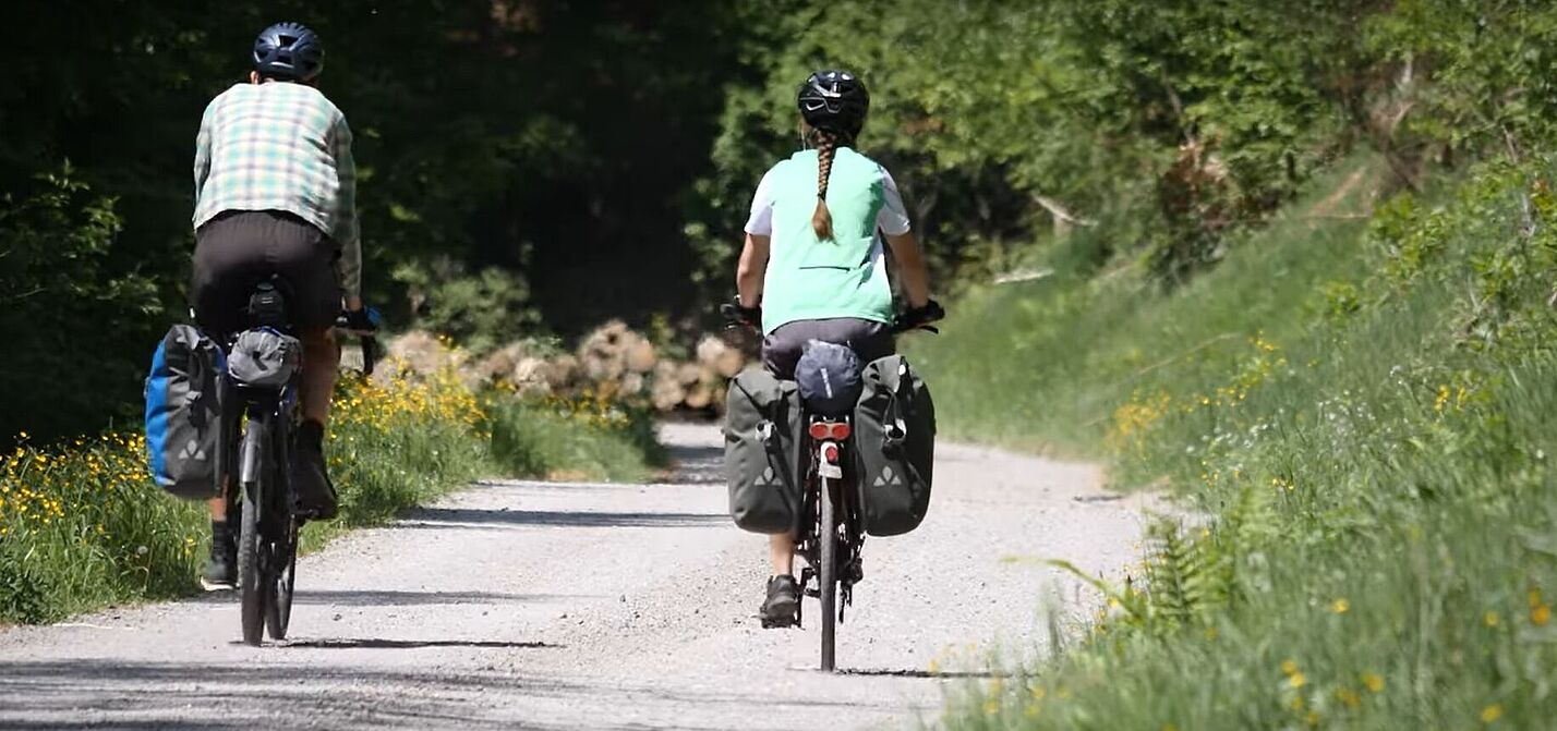Ein Mann und eine Frau fahren mit dem Fahrrad einen Waldweg entlang.