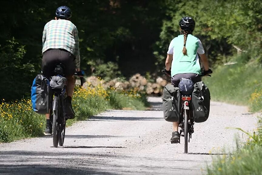Ein Mann und eine Frau fahren mit dem Fahrrad einen Waldweg entlang.