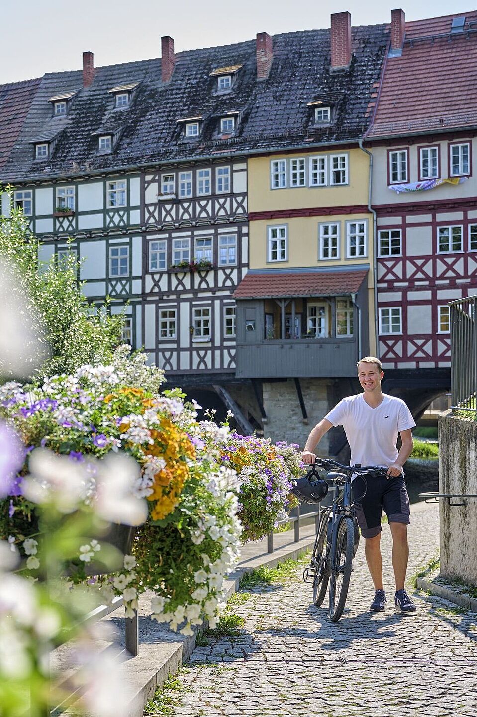 Städteketten-Attraktion: die Erfurter Krämerbrücke Ein Radfahrer steht vor der Erfurter Krämerbrücke. Im Vordergrund sind Blumen zu sehen.