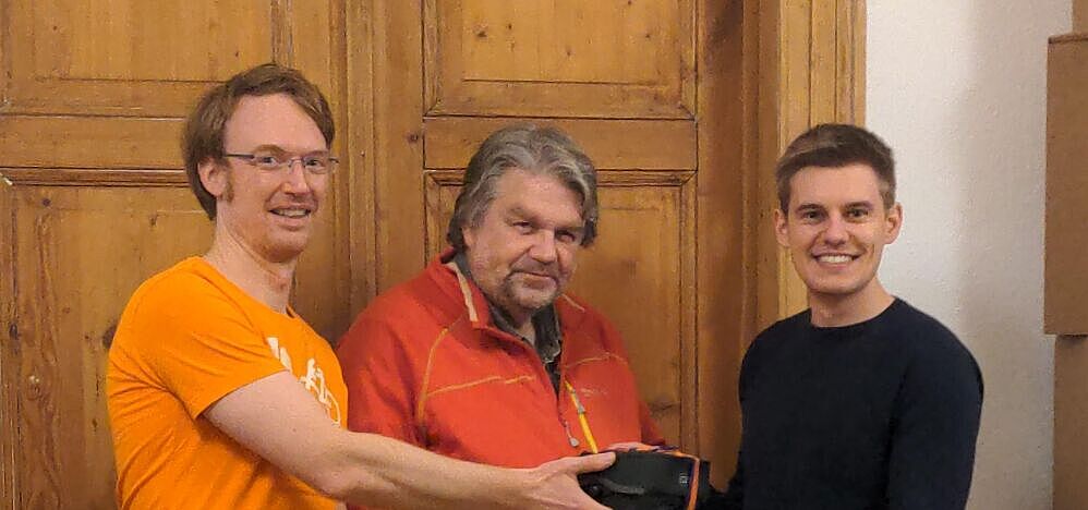 Drei Männer, von denen einer ein Geschenk überreicht bekommt.