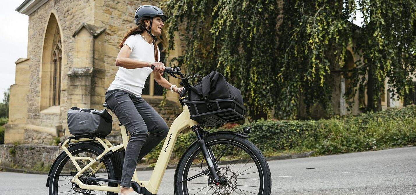 Fröhliche Frau fährt auf Elektrofahrrad, im Hintergrund eine Kirche. 