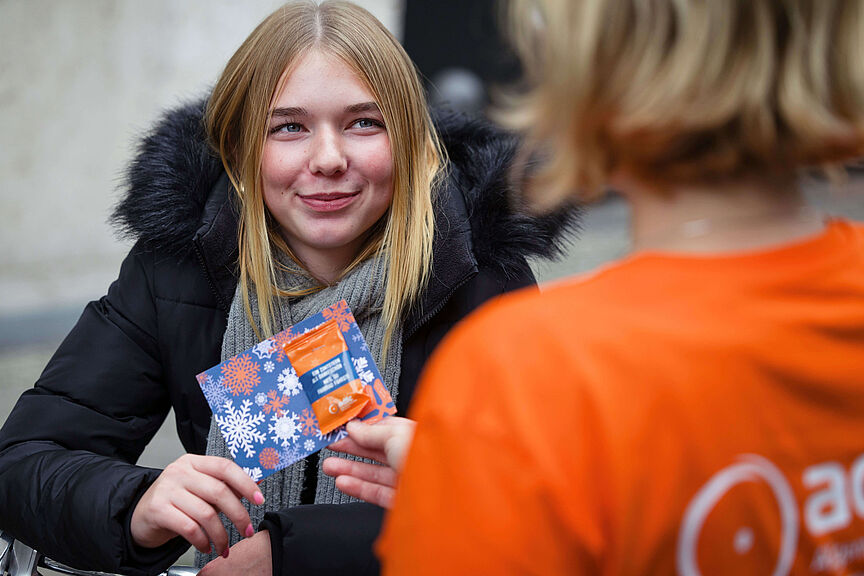 ADFC-Zimtstern-Aktion 2024 Eine lächelnde junge Frau in Winterjacke erhält von einer ADFC-Person eine blaue Karte mit Schneeflocken-Motiv und einen Zimtstern.