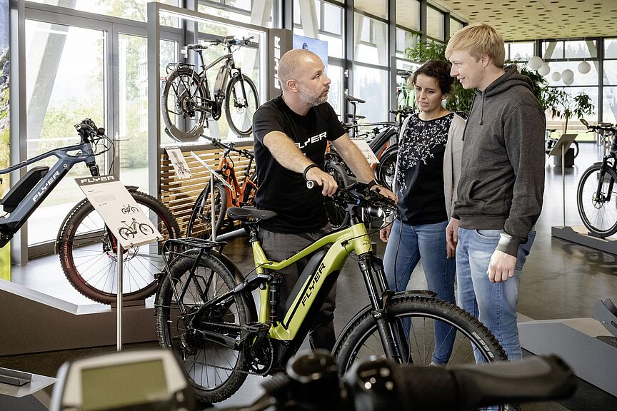 Showroom der Schweizer E-Bike-Pioniere Flyer. Showroom der Schweizer E-Bike-Pionierr Flyer. Mann steht vor Elektrofahrrad und berät eine Frau und einen Mann in einem Ladengeschäft.